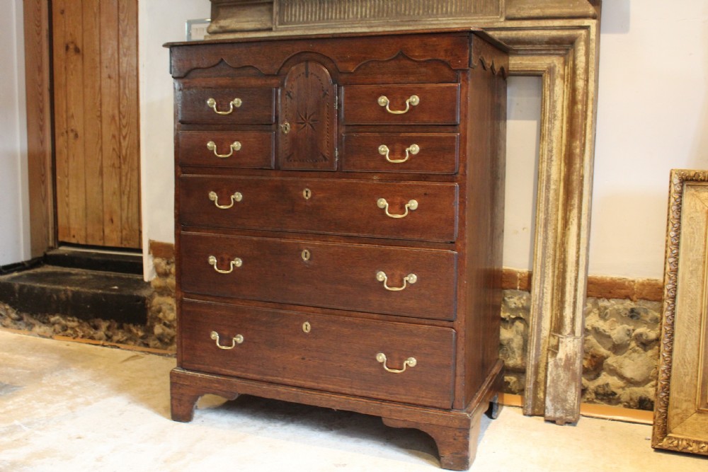 An 18th-century Georgian oak chest of drawers featuring brass swan-neck handles, a central carved arch door, and bracket feet. View XIV