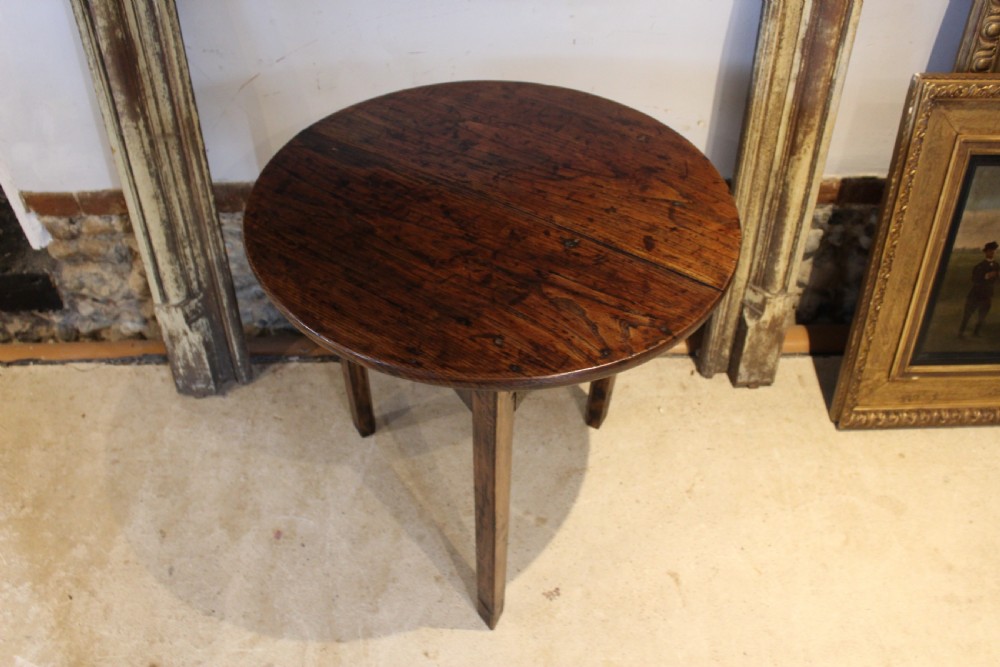 A George III circular elm cricket table featuring a dark planked timber top supported by three splayed wooden legs.