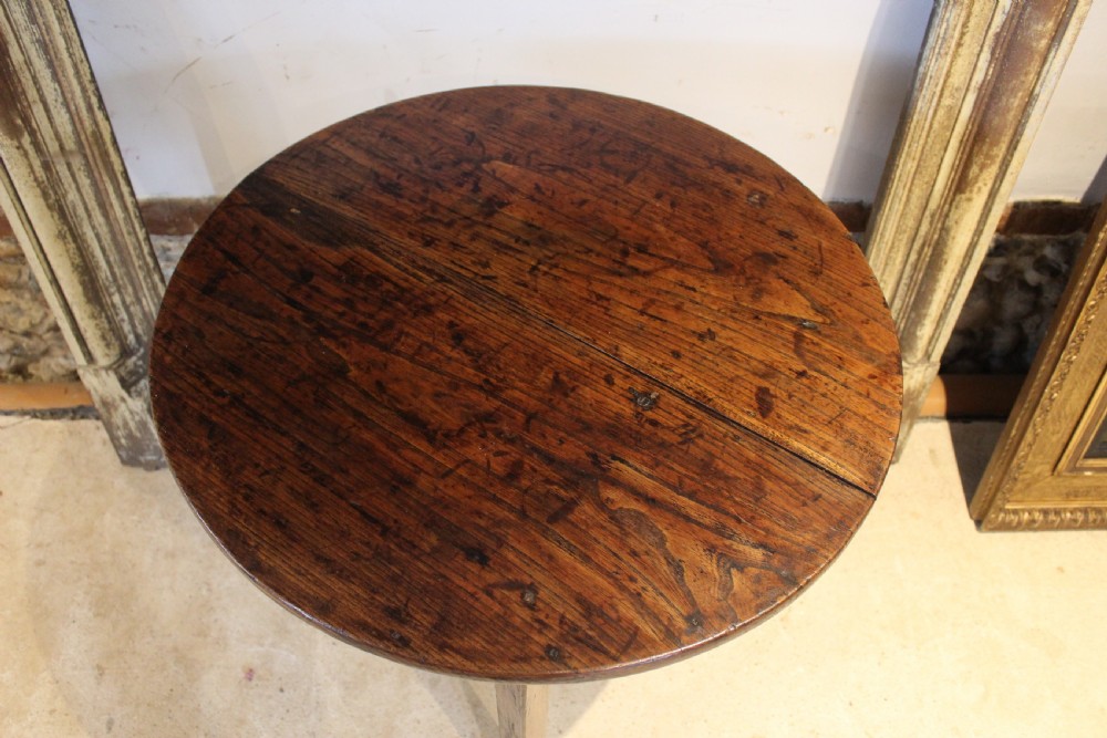 A George III circular elm cricket table featuring a dark planked timber top supported by three splayed wooden legs. View II