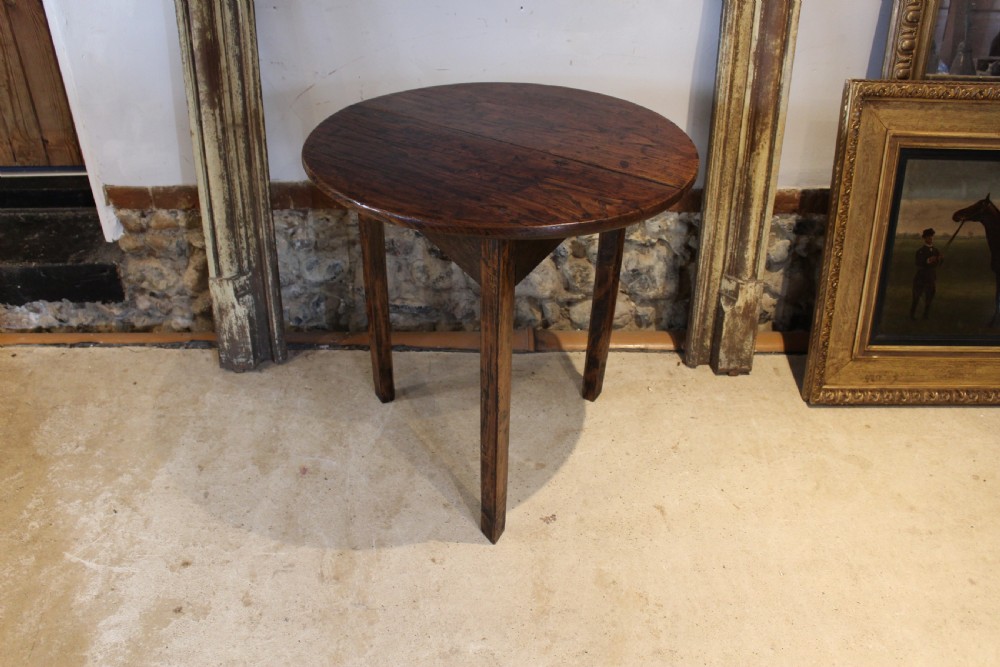 A George III circular elm cricket table featuring a dark planked timber top supported by three splayed wooden legs. View III