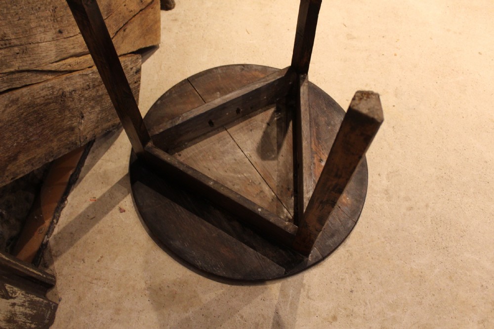 A George III circular elm cricket table featuring a dark planked timber top supported by three splayed wooden legs. View IV