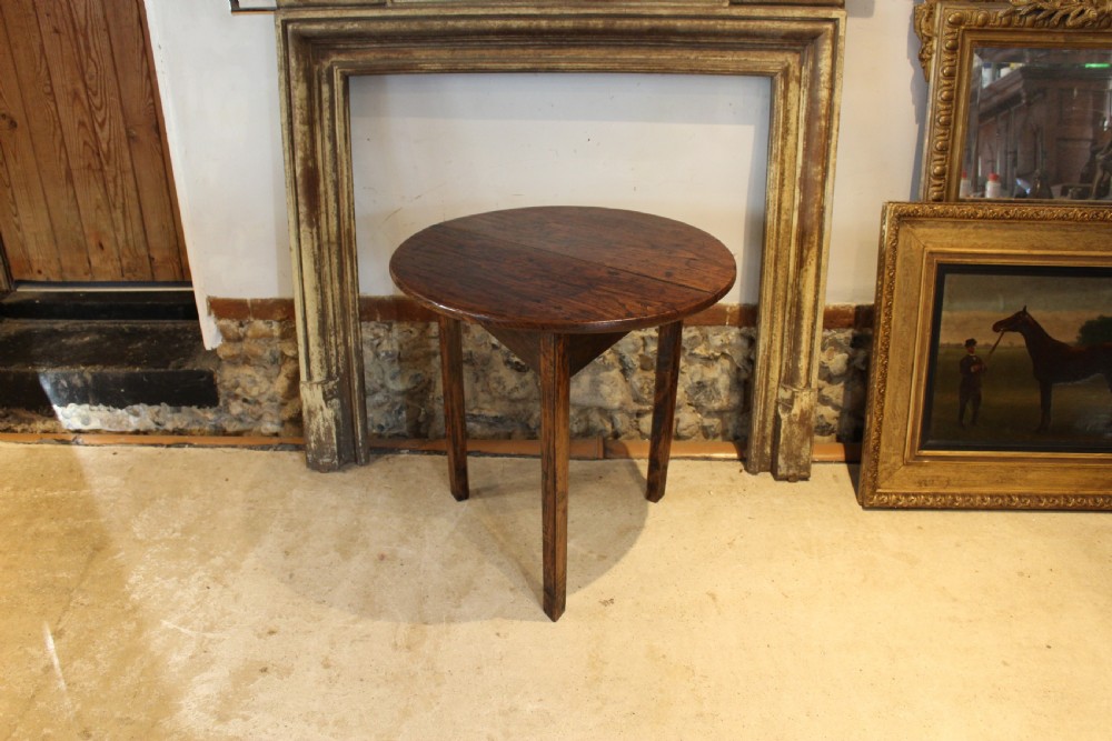 A George III circular elm cricket table featuring a dark planked timber top supported by three splayed wooden legs. View VII