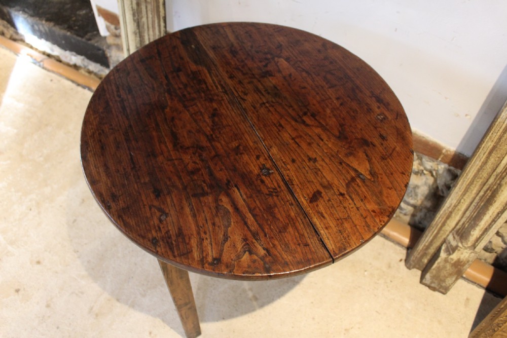 A George III circular elm cricket table featuring a dark planked timber top supported by three splayed wooden legs. View VIII