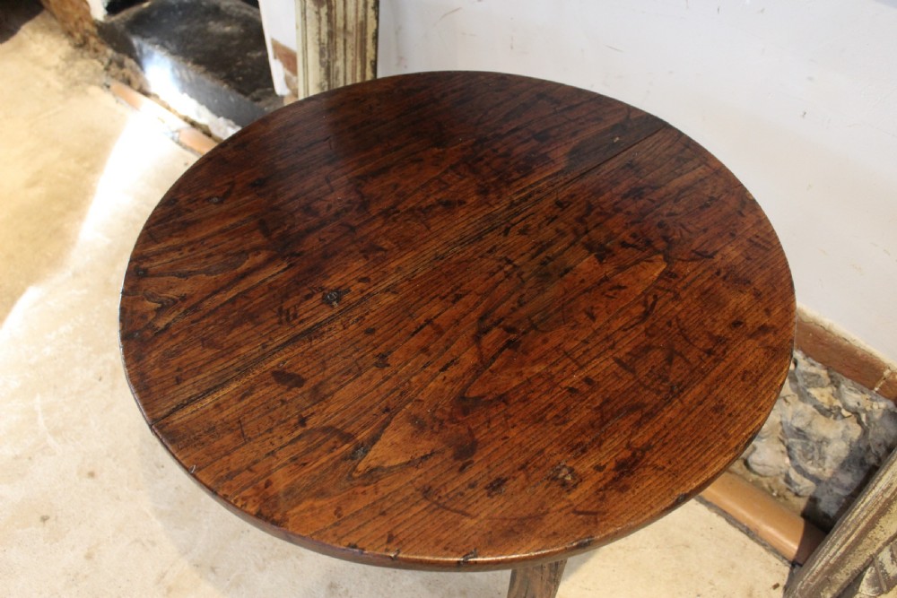 A George III circular elm cricket table featuring a dark planked timber top supported by three splayed wooden legs. View X