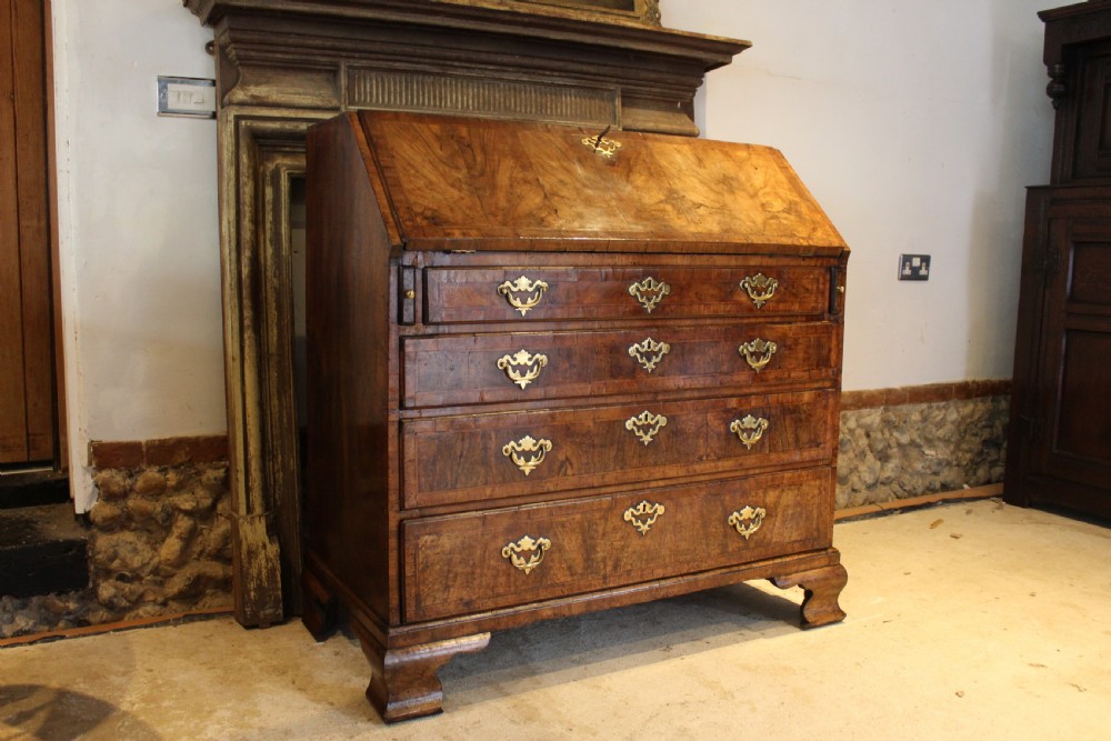 A George II walnut bureau featuring a slanted fall-front flap over four graduated drawers with brass handles, resting on bracket feet.