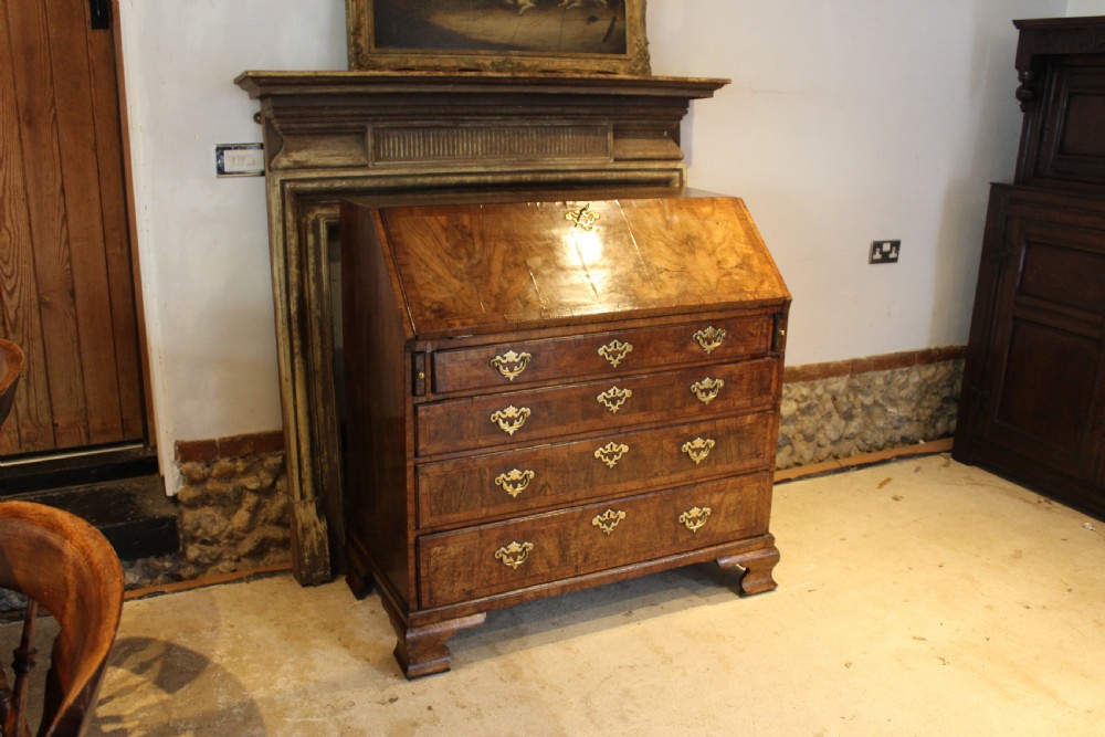 A George II walnut bureau featuring a slanted fall-front flap over four graduated drawers with brass handles, resting on bracket feet. View II