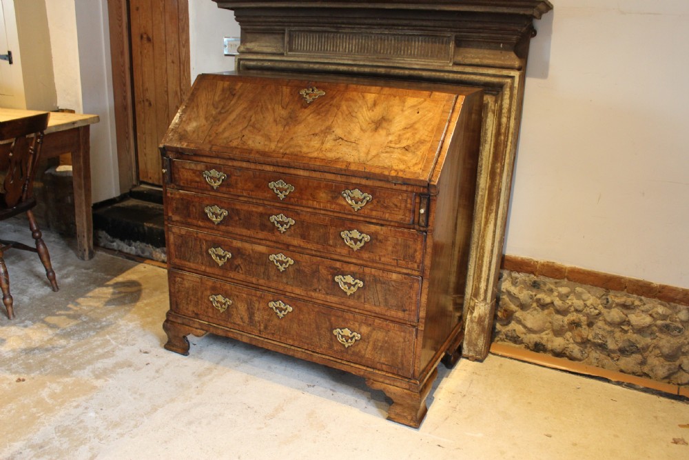 A George II walnut bureau featuring a slanted fall-front flap over four graduated drawers with brass handles, resting on bracket feet. View V