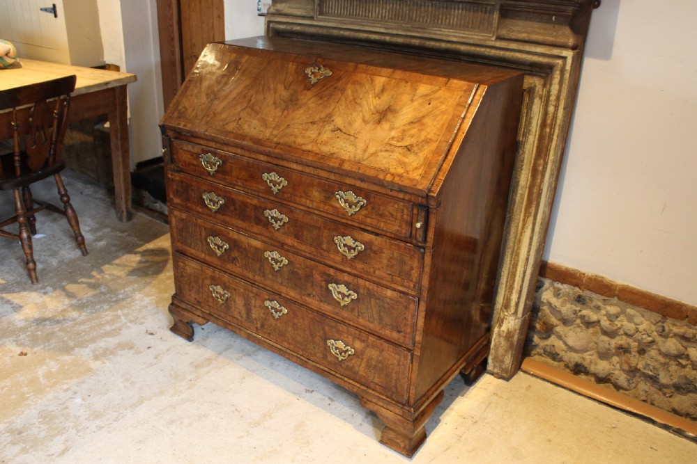 A George II walnut bureau featuring a slanted fall-front flap over four graduated drawers with brass handles, resting on bracket feet. View XII