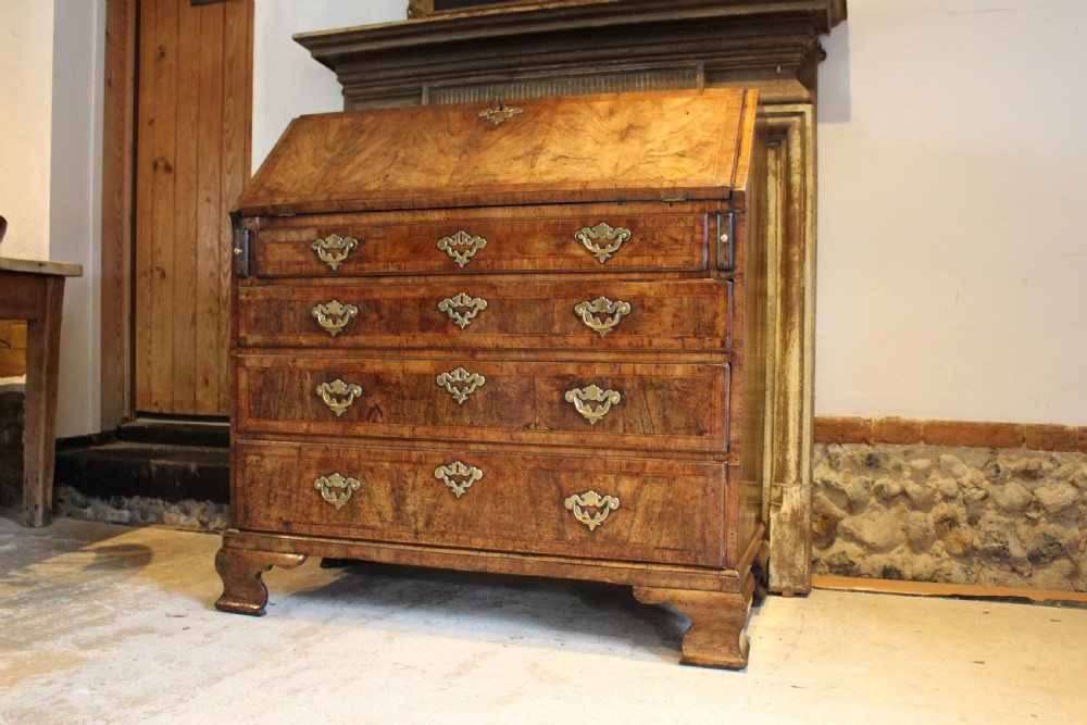 A George II walnut bureau featuring a slanted fall-front flap over four graduated drawers with brass handles, resting on bracket feet. View XVI