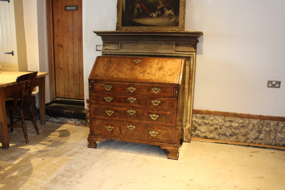 A George II walnut bureau featuring a slanted fall-front flap over four graduated drawers with brass handles, resting on bracket feet. View XVII