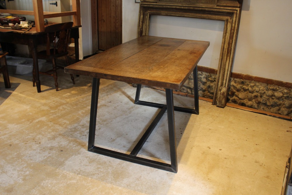 An antique George III oak plank table top with a warm brown patina mounted on a modern dark metal trapezoidal frame.
