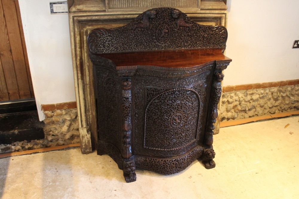 A late 19th-century dark padauk wood cabinet featuring intricate hand-carved pierced floral decoration, a carved gallery back, and lion-form supports.