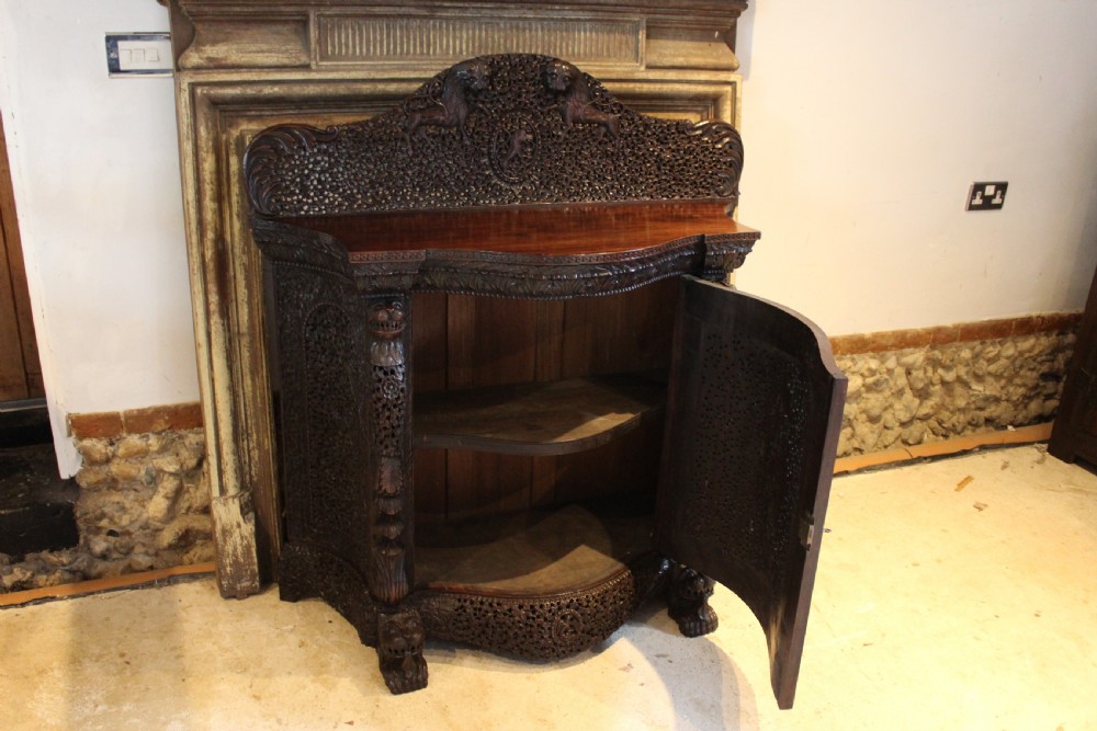 A late 19th-century dark padauk wood cabinet featuring intricate hand-carved pierced floral decoration, a carved gallery back, and lion-form supports. View VI