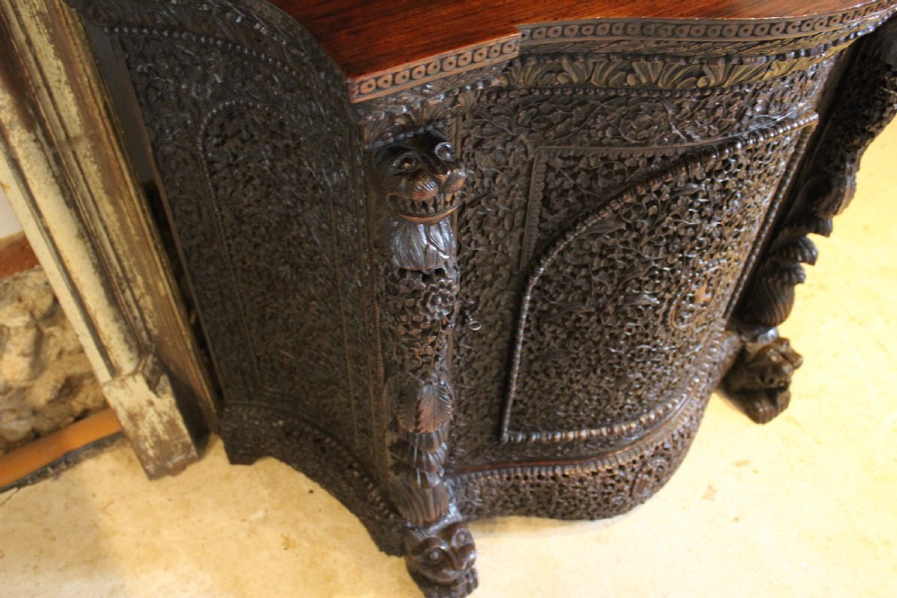 A late 19th-century dark padauk wood cabinet featuring intricate hand-carved pierced floral decoration, a carved gallery back, and lion-form supports. View IX