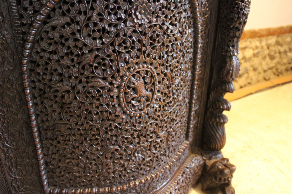 A late 19th-century dark padauk wood cabinet featuring intricate hand-carved pierced floral decoration, a carved gallery back, and lion-form supports. View X