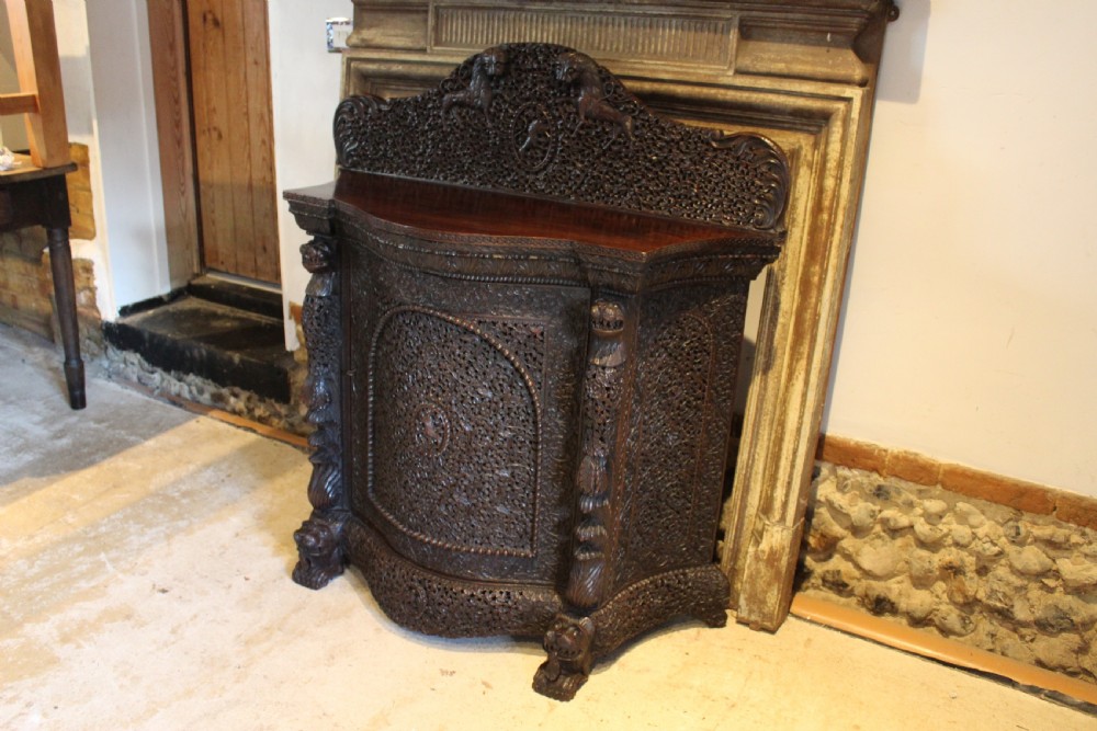 A late 19th-century dark padauk wood cabinet featuring intricate hand-carved pierced floral decoration, a carved gallery back, and lion-form supports. View XII