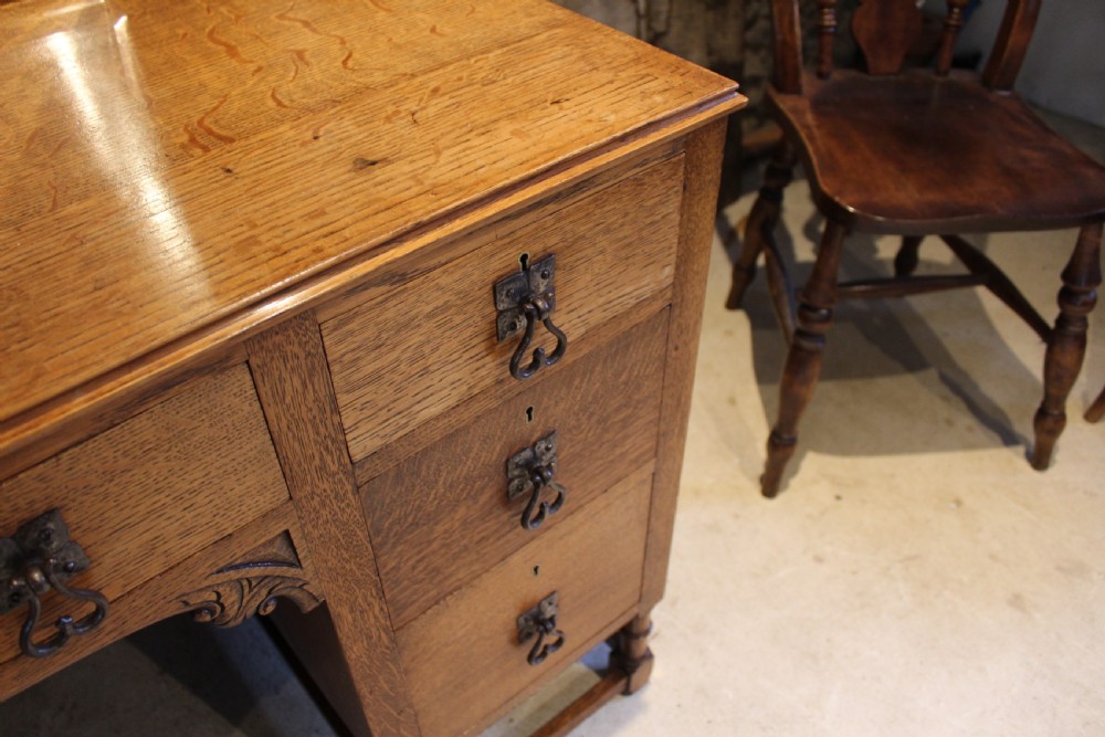 An Arts and Crafts solid oak dressing table featuring a central swinging mirror, carved spandrels, seven drawers with drop handles, and a kneehole stretcher base. View II