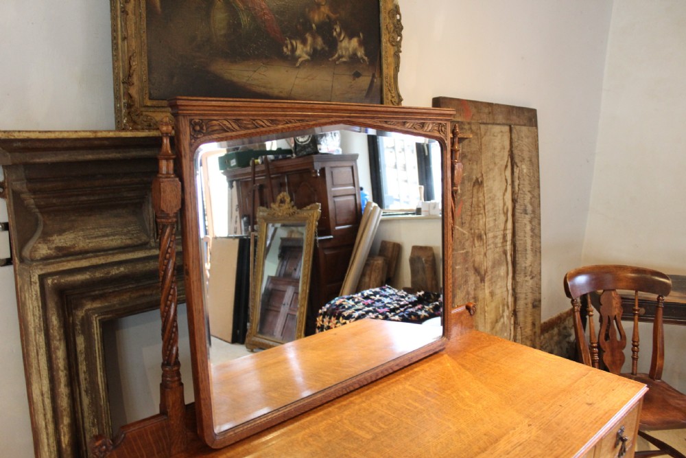 An Arts and Crafts solid oak dressing table featuring a central swinging mirror, carved spandrels, seven drawers with drop handles, and a kneehole stretcher base. View III