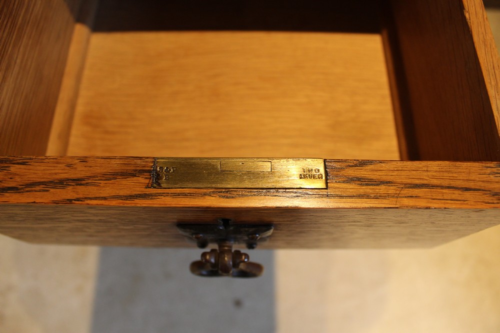 An Arts and Crafts solid oak dressing table featuring a central swinging mirror, carved spandrels, seven drawers with drop handles, and a kneehole stretcher base. View VIII