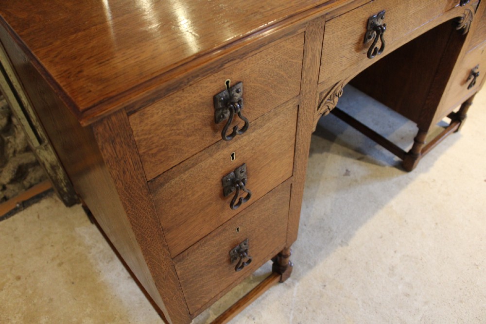 An Arts and Crafts solid oak dressing table featuring a central swinging mirror, carved spandrels, seven drawers with drop handles, and a kneehole stretcher base. View IX