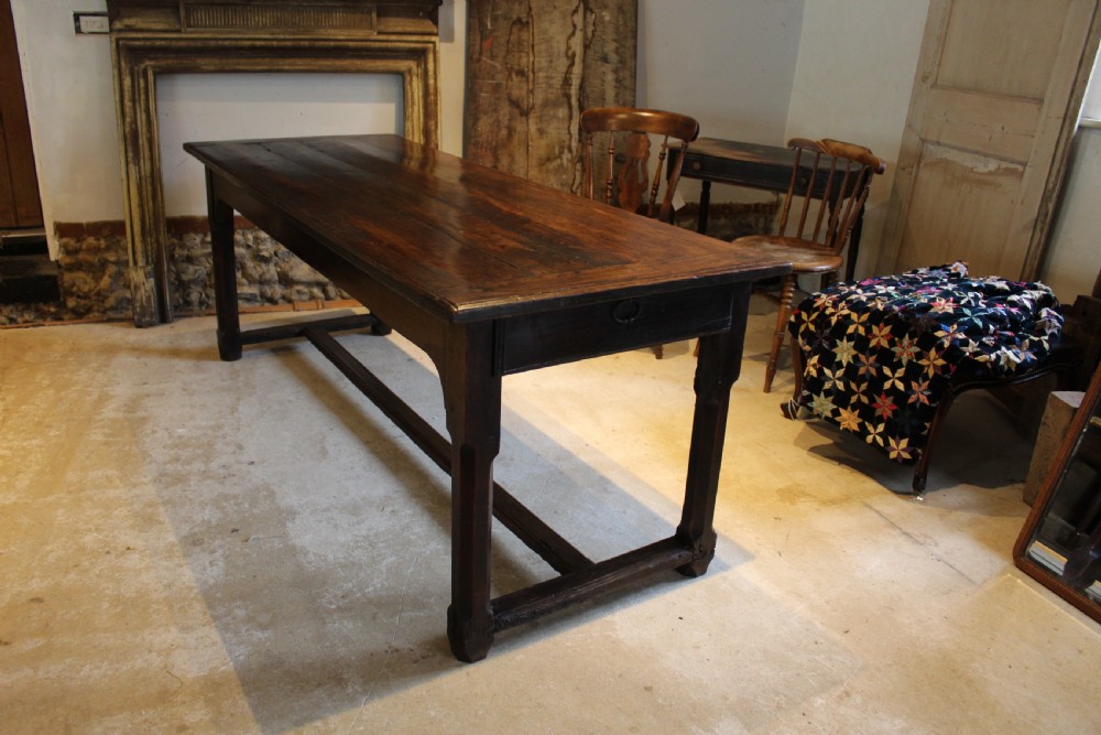 An 18th-century dark oak refectory dining table featuring a plank top, single end drawer, and square legs joined by a perimeter stretcher. View IV