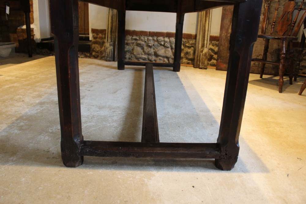 An 18th-century dark oak refectory dining table featuring a plank top, single end drawer, and square legs joined by a perimeter stretcher. View V