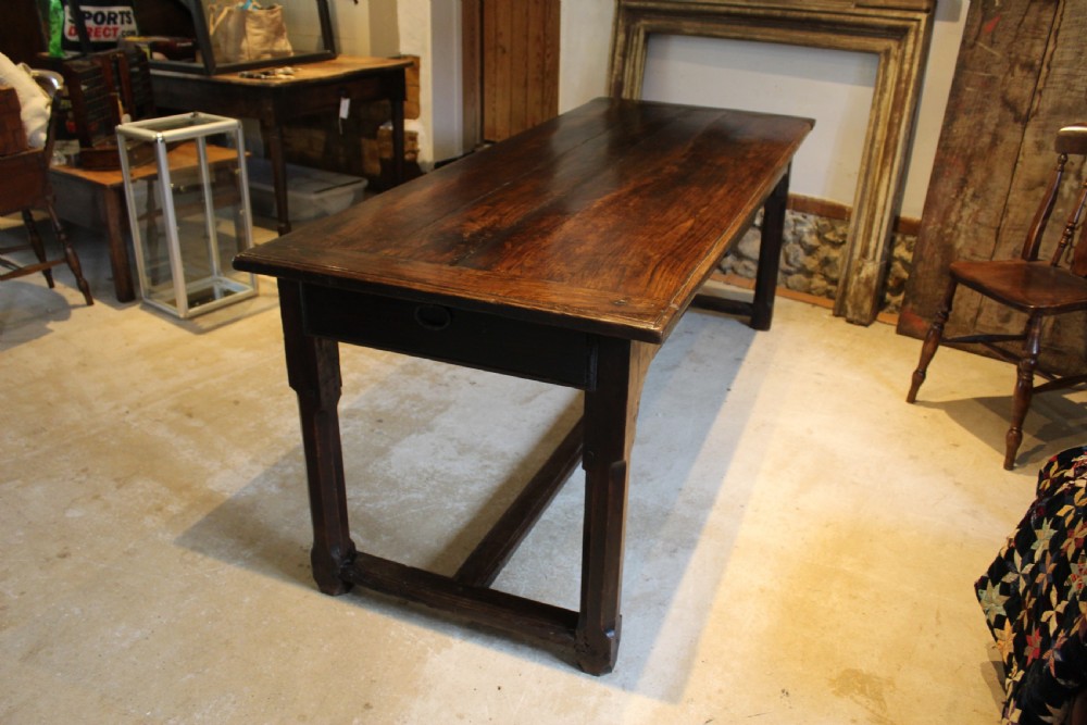 An 18th-century dark oak refectory dining table featuring a plank top, single end drawer, and square legs joined by a perimeter stretcher. View VII