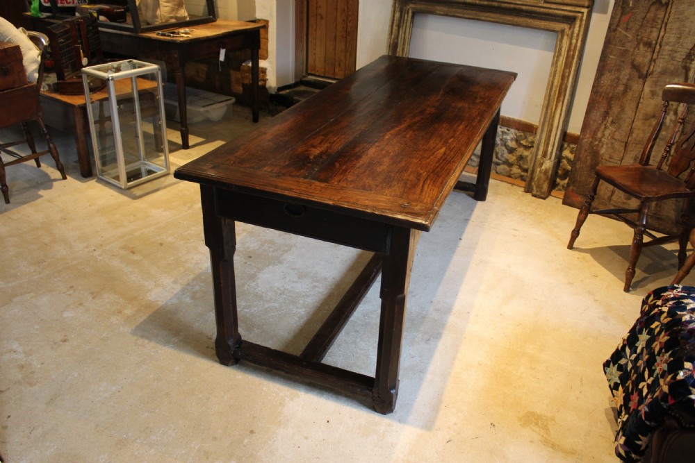An 18th-century dark oak refectory dining table featuring a plank top, single end drawer, and square legs joined by a perimeter stretcher. View X