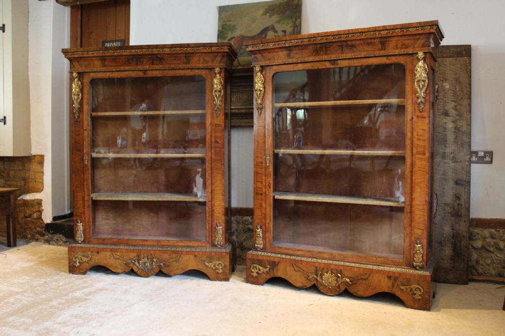A pair of 19th-century Victorian walnut display cabinets featuring glazed single doors, adjustable interior shelves, and ornate gilt-bronze mounts on the corners and base. View II