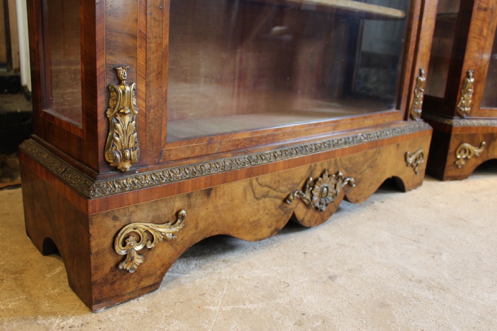 A pair of 19th-century Victorian walnut display cabinets featuring glazed single doors, adjustable interior shelves, and ornate gilt-bronze mounts on the corners and base. View VII