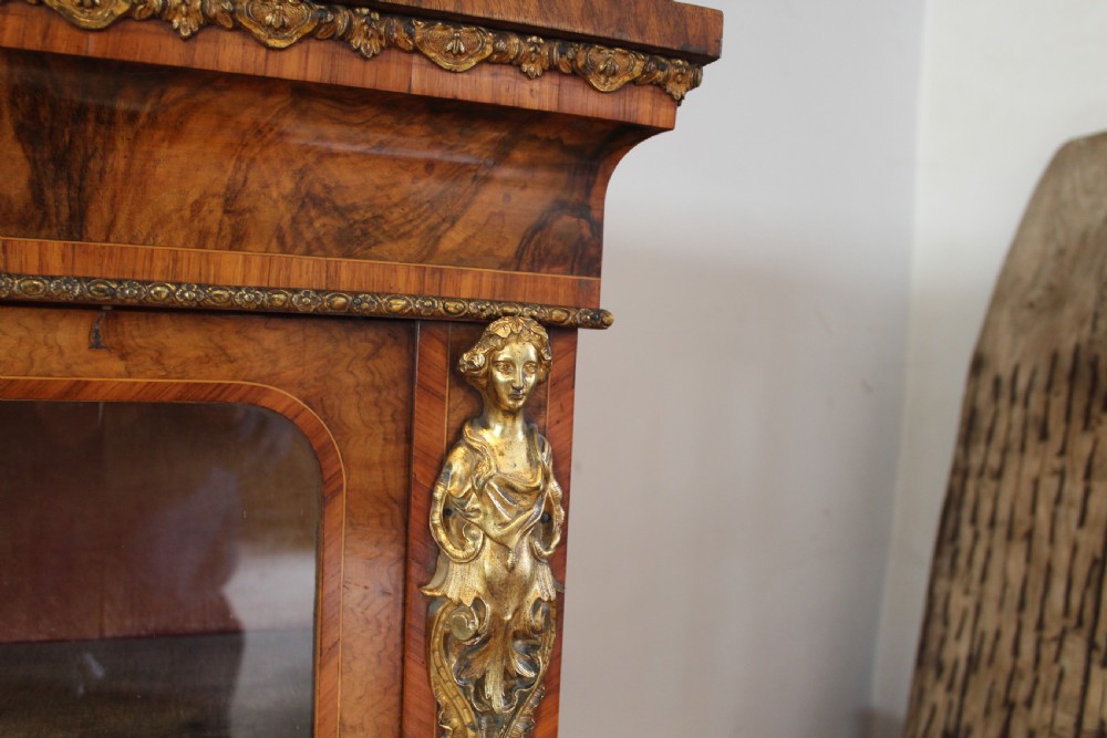 A pair of 19th-century Victorian walnut display cabinets featuring glazed single doors, adjustable interior shelves, and ornate gilt-bronze mounts on the corners and base. View VIII
