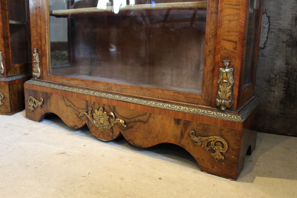 A pair of 19th-century Victorian walnut display cabinets featuring glazed single doors, adjustable interior shelves, and ornate gilt-bronze mounts on the corners and base. View IX
