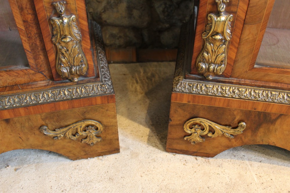 A pair of 19th-century Victorian walnut display cabinets featuring glazed single doors, adjustable interior shelves, and ornate gilt-bronze mounts on the corners and base. View XIII