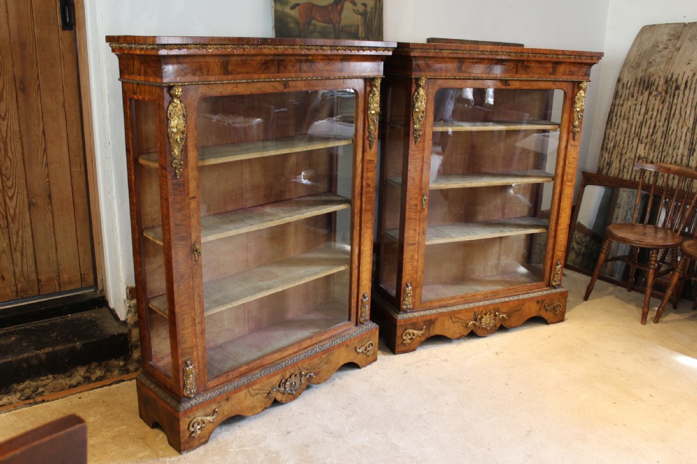 A pair of 19th-century Victorian walnut display cabinets featuring glazed single doors, adjustable interior shelves, and ornate gilt-bronze mounts on the corners and base. View XIV