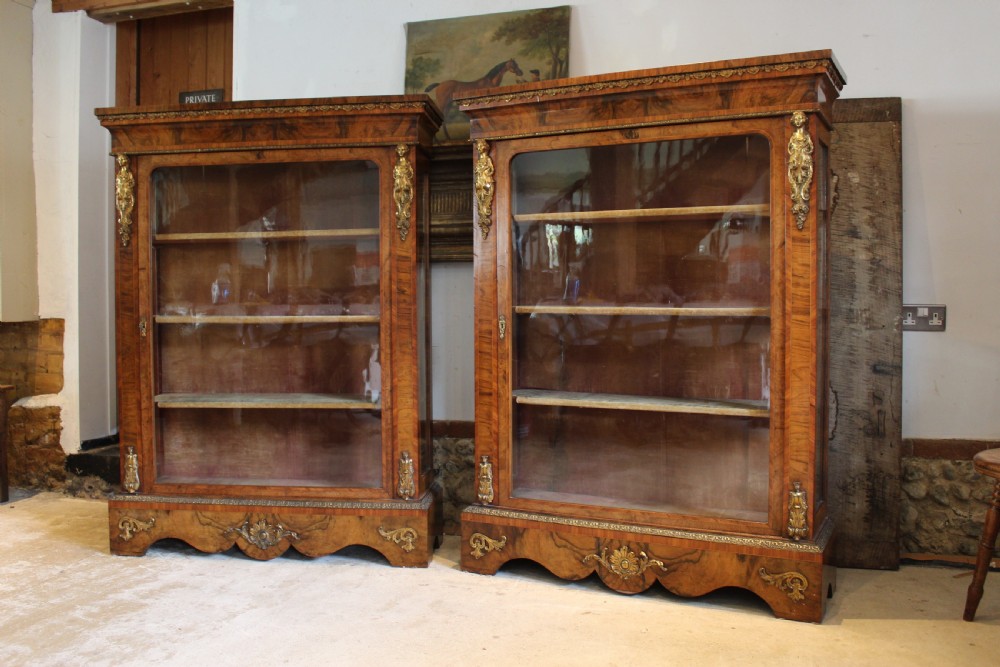 A pair of 19th-century Victorian walnut display cabinets featuring glazed single doors, adjustable interior shelves, and ornate gilt-bronze mounts on the corners and base. View XVII