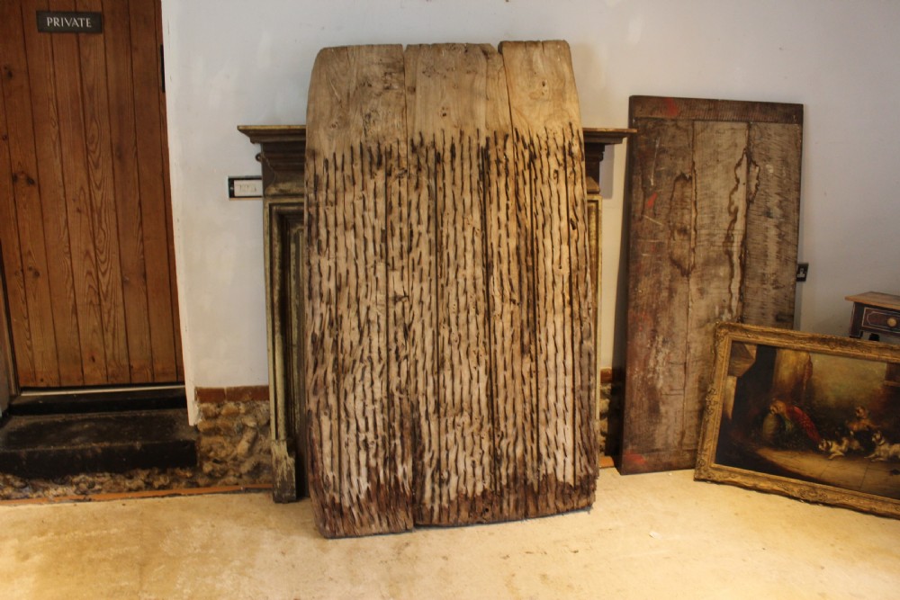 An 18th century elm wood threshing board with embedded dark flint stones leaning vertically against an interior wall.