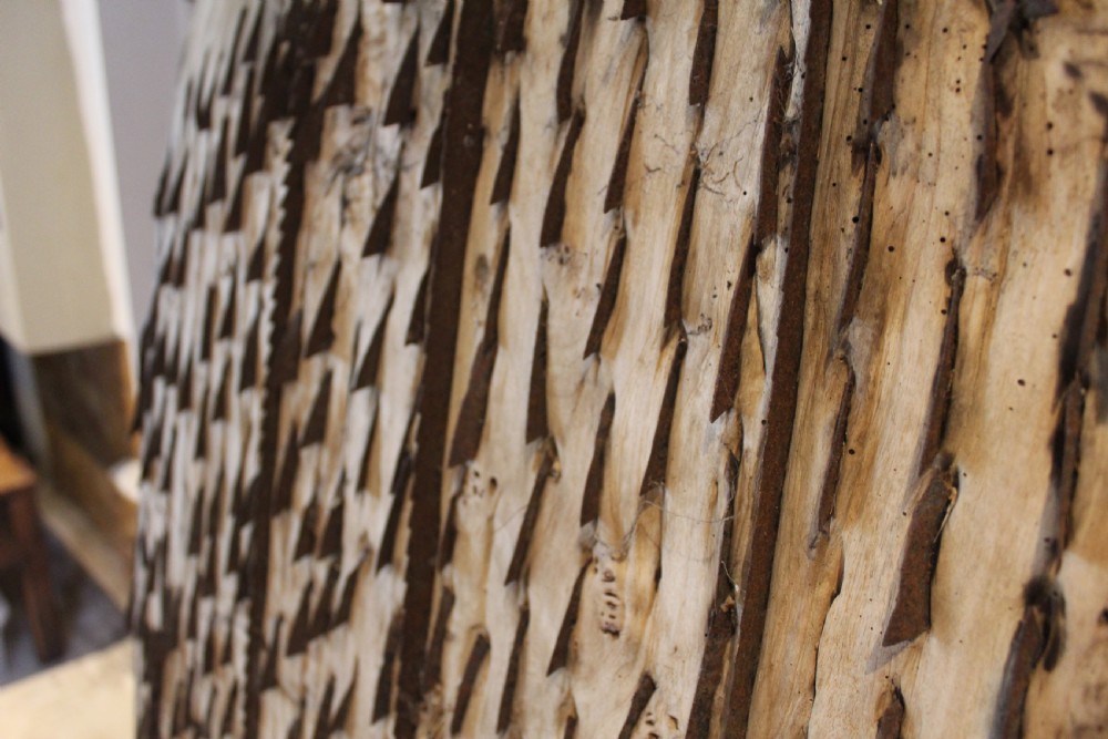 An 18th century elm wood threshing board with embedded dark flint stones leaning vertically against an interior wall. View II