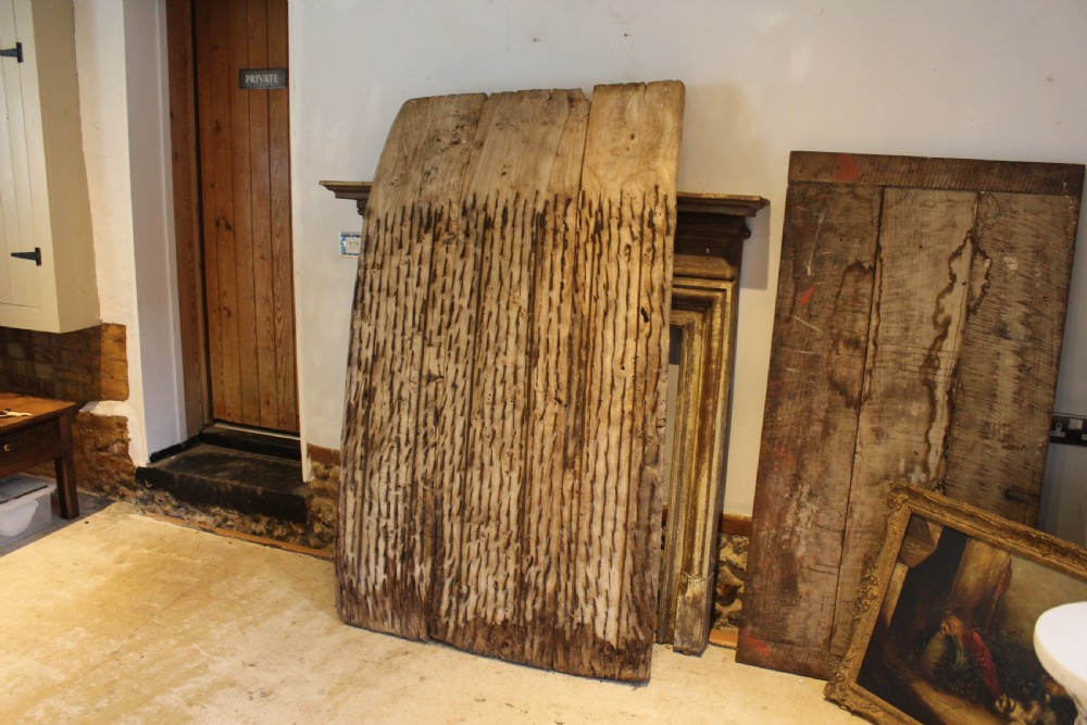 An 18th century elm wood threshing board with embedded dark flint stones leaning vertically against an interior wall. View VI