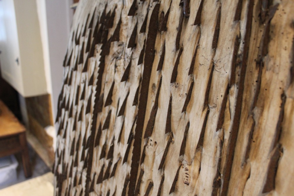 An 18th century elm wood threshing board with embedded dark flint stones leaning vertically against an interior wall. View VII