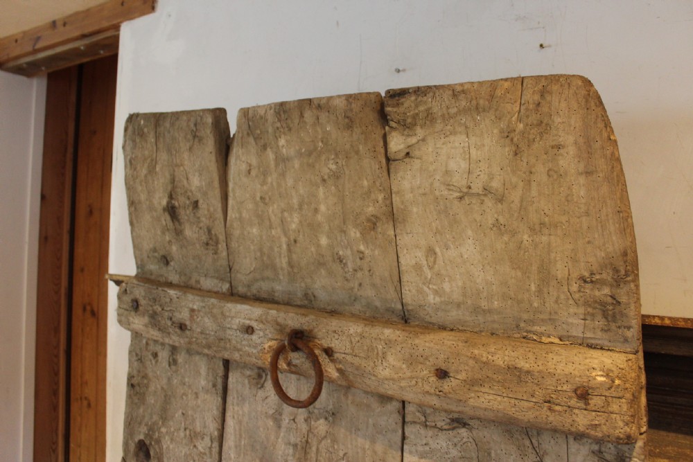An 18th century elm wood threshing board with embedded dark flint stones leaning vertically against an interior wall. View X