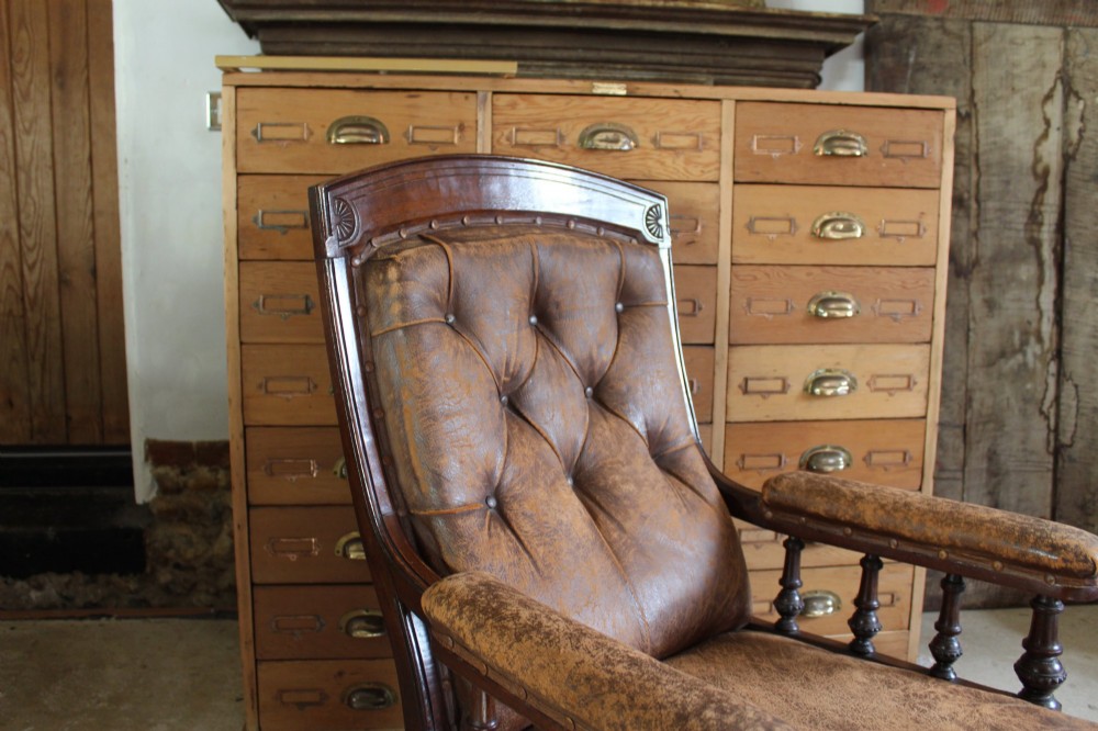 A late Victorian walnut armchair featuring button-backed brown leather upholstery, turned spindle arm supports, stud detailing, and carved front legs on castors. View III