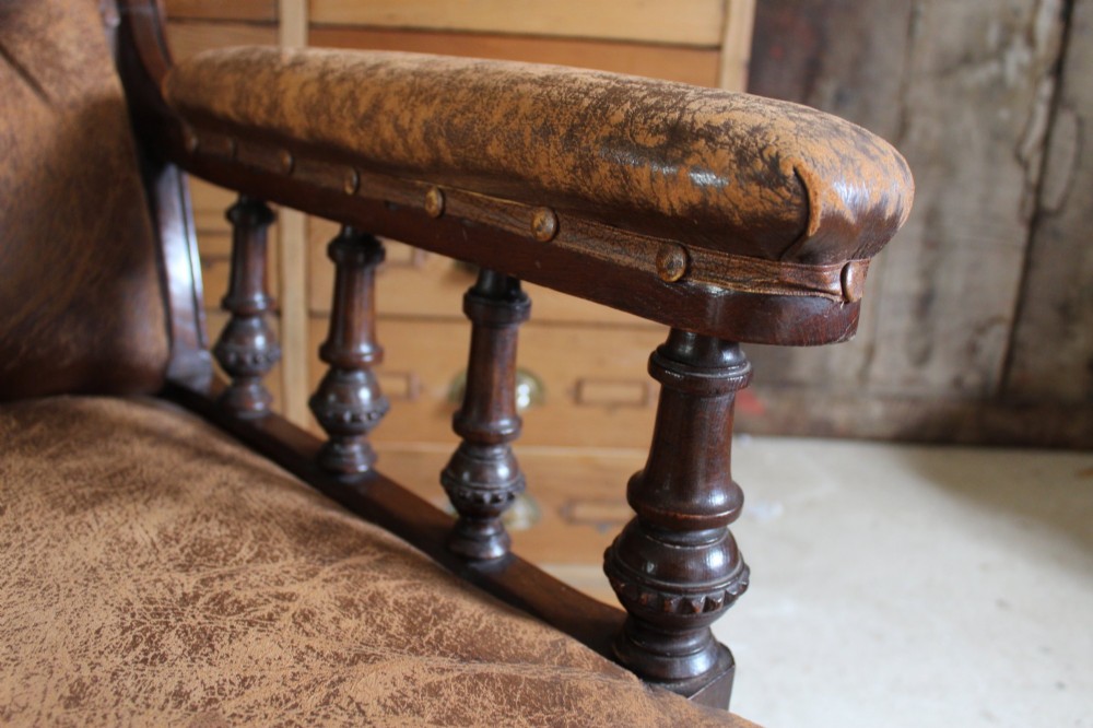 A late Victorian walnut armchair featuring button-backed brown leather upholstery, turned spindle arm supports, stud detailing, and carved front legs on castors. View IV