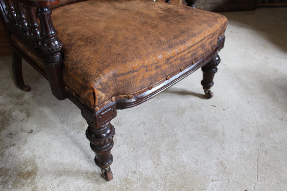 A late Victorian walnut armchair featuring button-backed brown leather upholstery, turned spindle arm supports, stud detailing, and carved front legs on castors. View VI