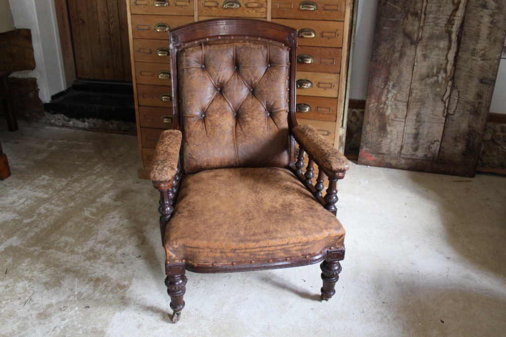 A late Victorian walnut armchair featuring button-backed brown leather upholstery, turned spindle arm supports, stud detailing, and carved front legs on castors. View VIII