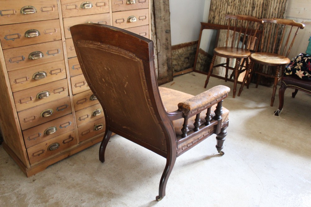A late Victorian walnut armchair featuring button-backed brown leather upholstery, turned spindle arm supports, stud detailing, and carved front legs on castors. View XI