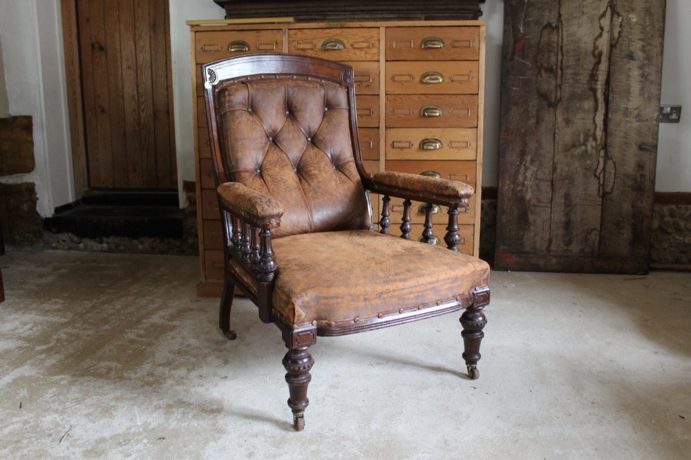 A late Victorian walnut armchair featuring button-backed brown leather upholstery, turned spindle arm supports, stud detailing, and carved front legs on castors. View XIV