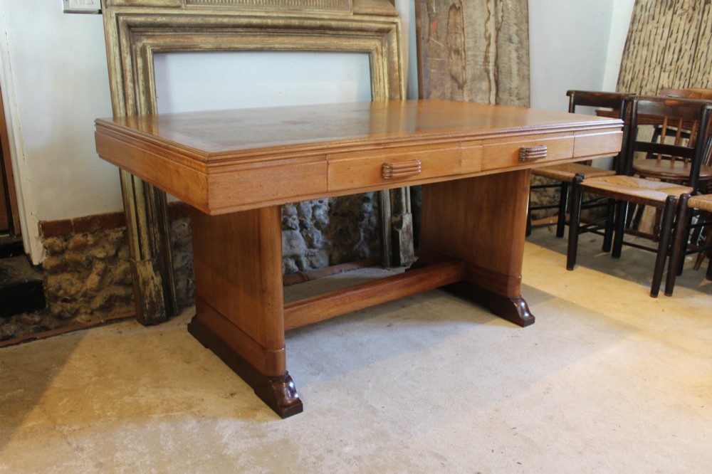 An Art Deco walnut desk featuring a rectangular top with an inset writing surface, frieze drawers with ribbed handles, and a trestle-style base with a low stretcher. View X