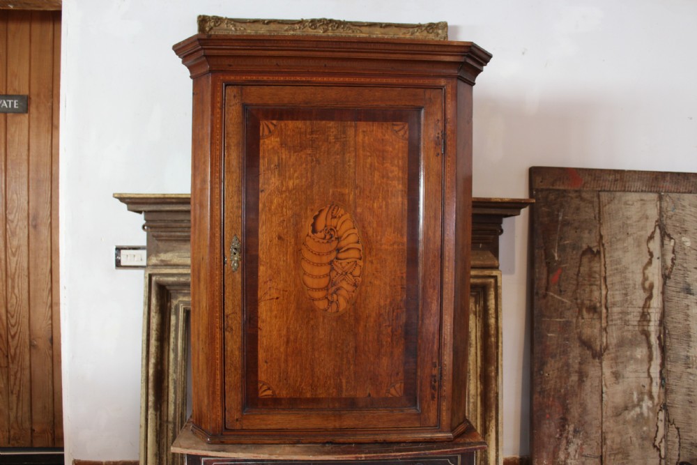 An 18th-century Georgian oak corner cupboard featuring a central inlaid shell motif on the single panel door and decorative crossbanding.