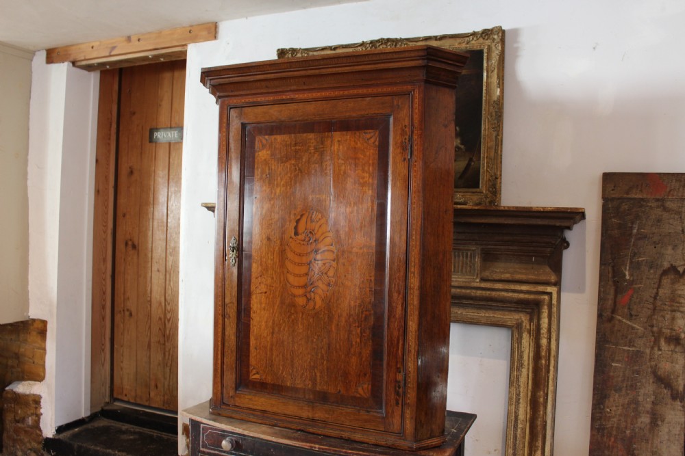 An 18th-century Georgian oak corner cupboard featuring a central inlaid shell motif on the single panel door and decorative crossbanding. View VII