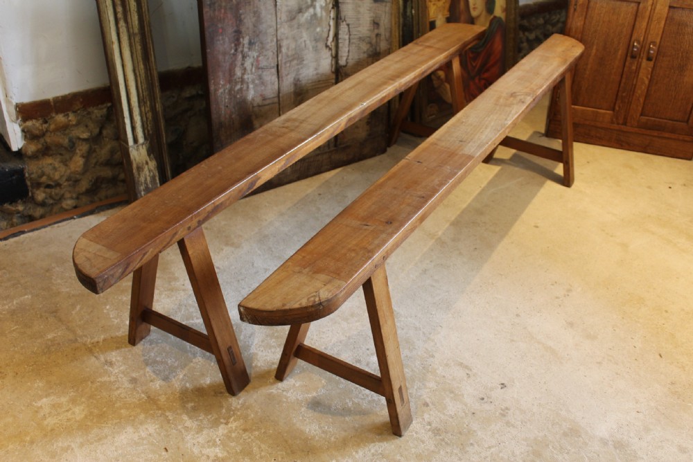 A pair of long 19th-century French fruitwood refectory benches featuring A-frame trestle legs and pegged joinery.